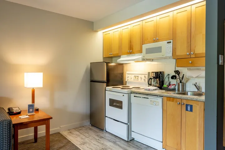 Kitchen featuring white appliances, tasteful backsplash, light wood-style flooring, under cabinet range hood, and light countertops