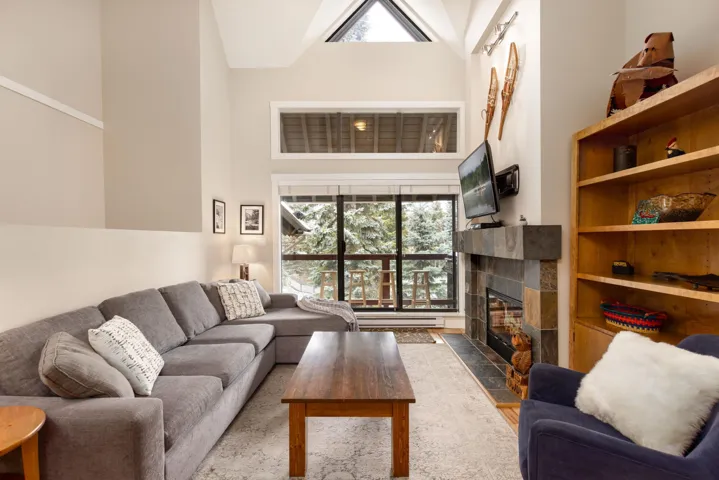 Living room with a high ceiling, a tiled fireplace, and light wood finished floors