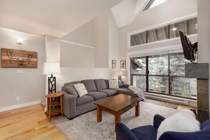 Living area featuring light wood-type flooring, a baseboard heating unit, plenty of natural light, and a high ceiling