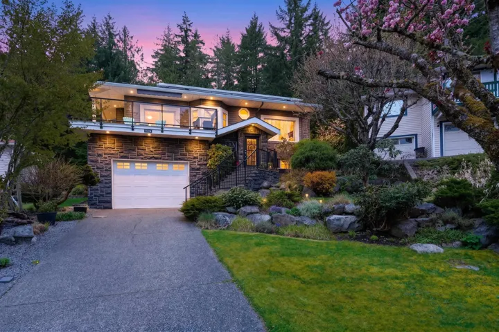 Modern home featuring stone siding, driveway, a garage, a yard, and a balcony