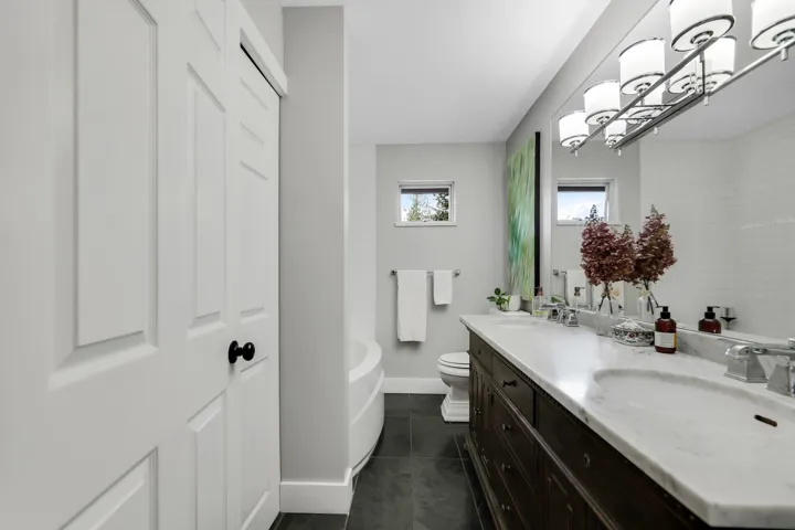 Full bathroom with double vanity, dark tile patterned flooring, and a tub