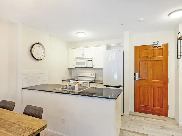 Kitchen with dark countertops, white appliances, tasteful backsplash, white cabinetry, and a peninsula