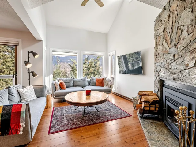 Living area featuring wood-type flooring, high vaulted ceiling, baseboards, a ceiling fan, and a fireplace