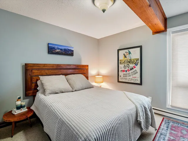 Carpeted bedroom with beamed ceiling, a textured ceiling, and baseboard heating