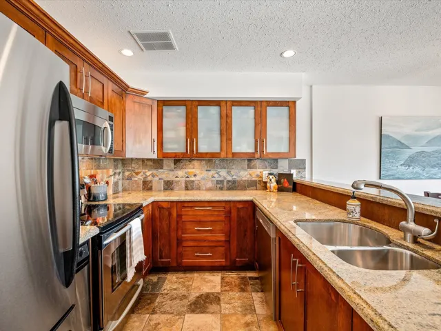 Kitchen featuring light stone counters, a sink, appliances with stainless steel finishes, visible vents, and decorative backsplash