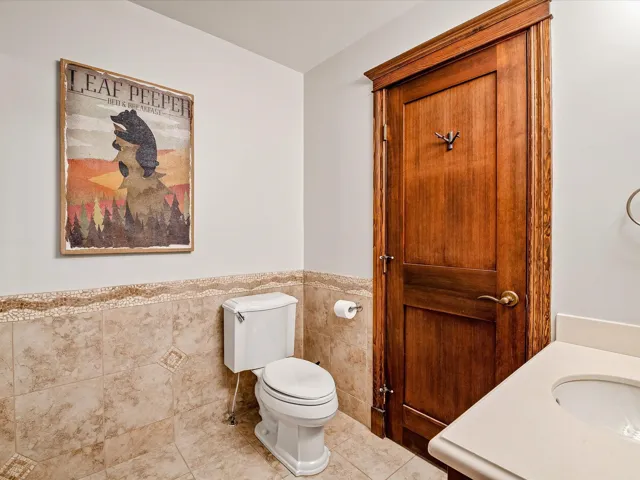 Half bathroom with tile patterned flooring, tile walls, toilet, a sink, and wainscoting