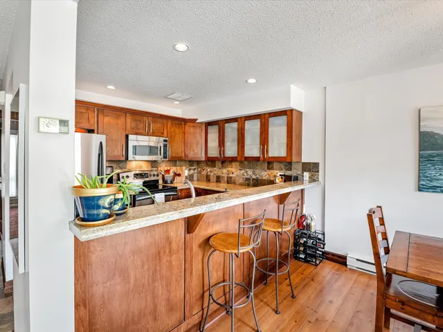 Kitchen with a kitchen bar, tasteful backsplash, light wood-style flooring, appliances with stainless steel finishes, and glass insert cabinets