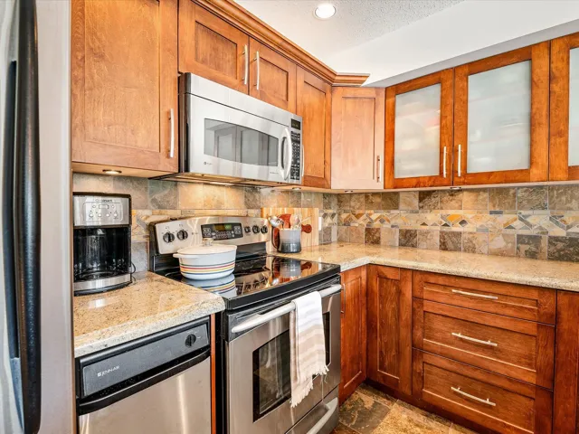 Kitchen featuring glass insert cabinets, brown cabinetry, stainless steel appliances, and backsplash