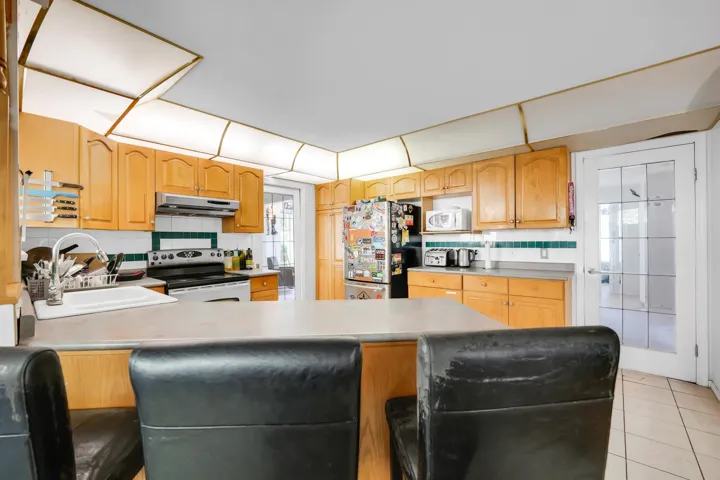 Kitchen featuring electric stove, a sink, white microwave, under cabinet range hood, and freestanding refrigerator
