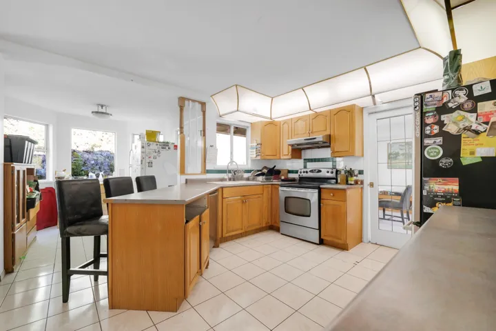 Kitchen featuring a sink, light tile patterned flooring, appliances with stainless steel finishes, a peninsula, and under cabinet range hood