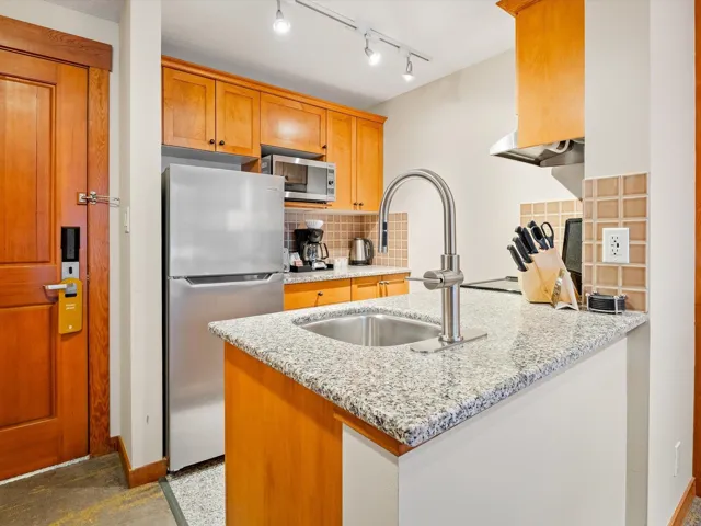 Kitchen with a sink, backsplash, stainless steel appliances, a peninsula, and light stone countertops