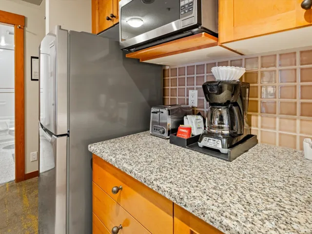 Kitchen with brown cabinets, light stone counters, appliances with stainless steel finishes, a toaster, and decorative backsplash