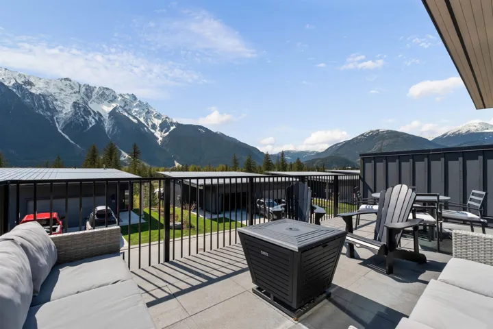 Expansive rooftop patio with mountain backdrop, featuring black metal railings and concrete-style pavers