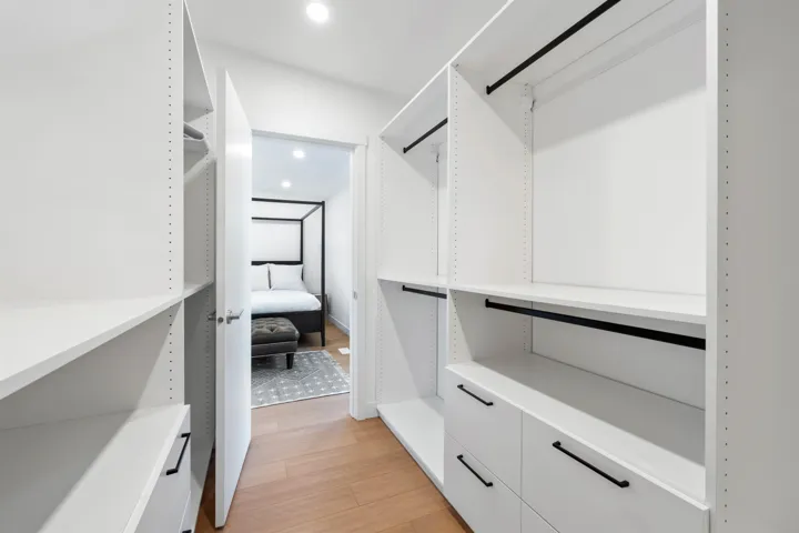 Custom closet system featuring white shelving, integrated drawers with black hardware, and wood-finish flooring