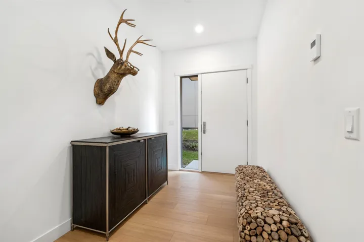 Light wood-finish flooring with a white wall finish, recessed lighting, and a modern entrance door