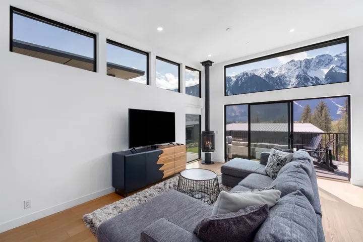 High ceilings with multiple large windows, a freestanding black stove, light wood-finish flooring, and a sliding glass door leading to a balcony