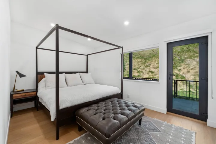Recessed lighting, light wood-finish flooring, white walls, black-framed window, and a black-framed glass door with exterior balcony