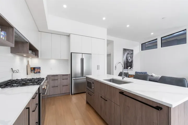 Modern kitchen featuring a gas range, stainless steel appliances, large center island with integrated sink, wood-finish flooring, and crisp white cabinetry