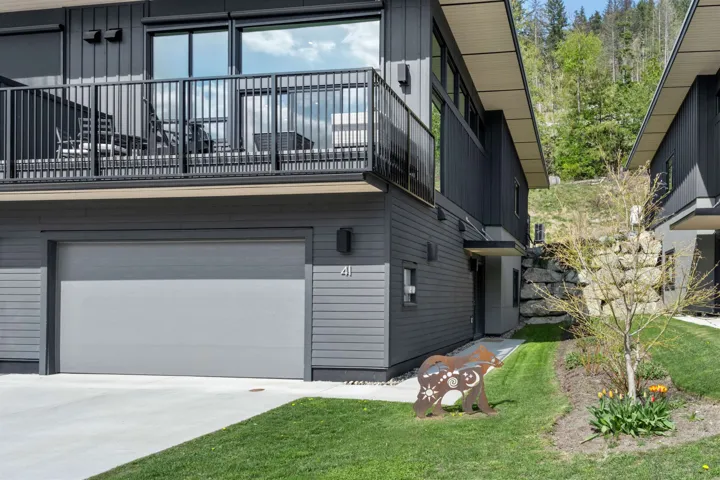 Contemporary exterior featuring dark siding, an upper-level balcony with metal railings, an integrated garage, and a concrete driveway