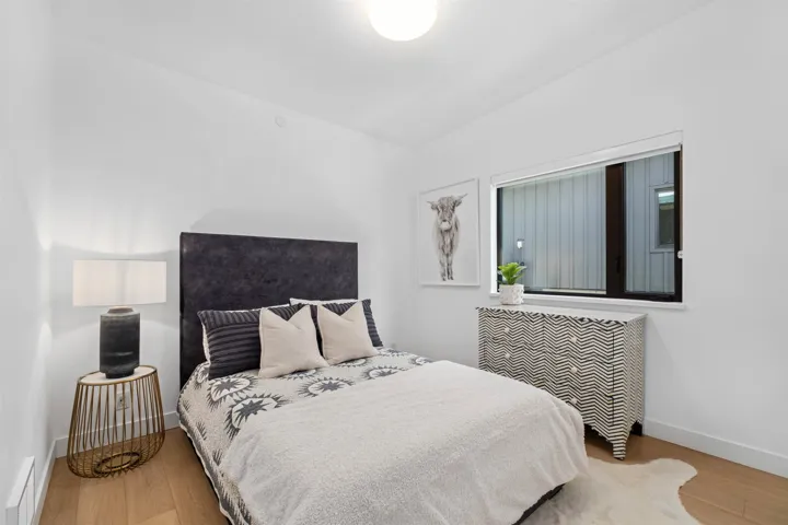 Recessed lighting, light wood-finish flooring, white walls, dark upholstered headboard, and a large horizontal window