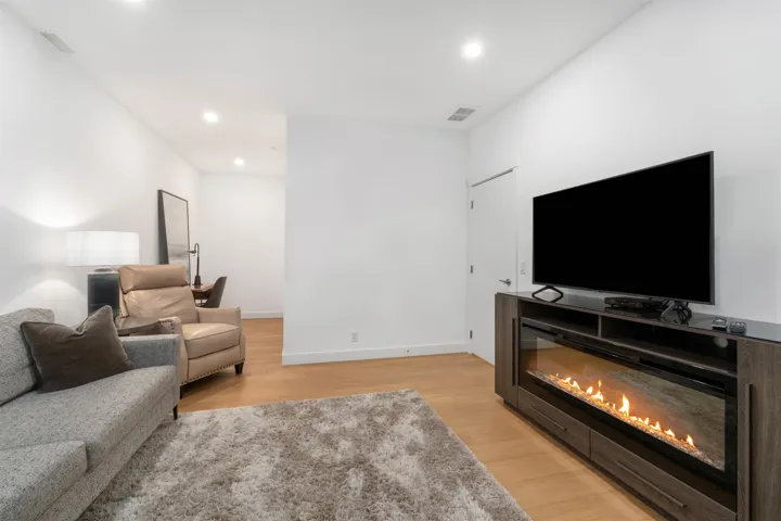 Integrated linear fireplace entertainment console with storage, wood-finish flooring, and recessed ceiling lighting