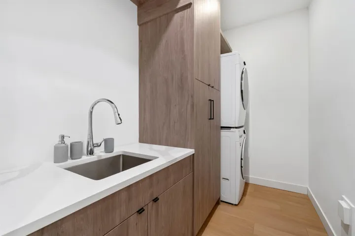 Laundry area featuring wood-finish cabinetry, white countertop, stainless steel sink, and stackable washer/dryer