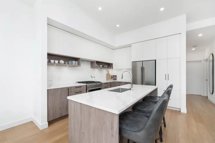 Modern kitchen featuring an integrated stainless steel refrigerator, a large center island with an undermount sink, a gas range, and wood-finish cabinetry