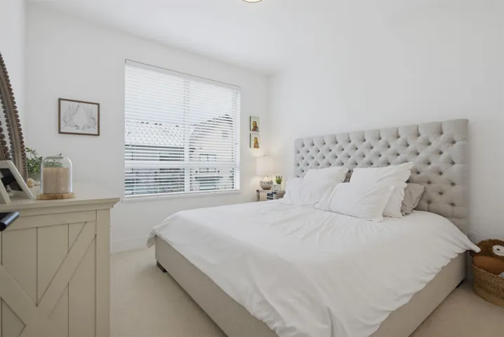 Bright bedroom featuring white walls, a large window with horizontal blinds, and light-colored carpeting