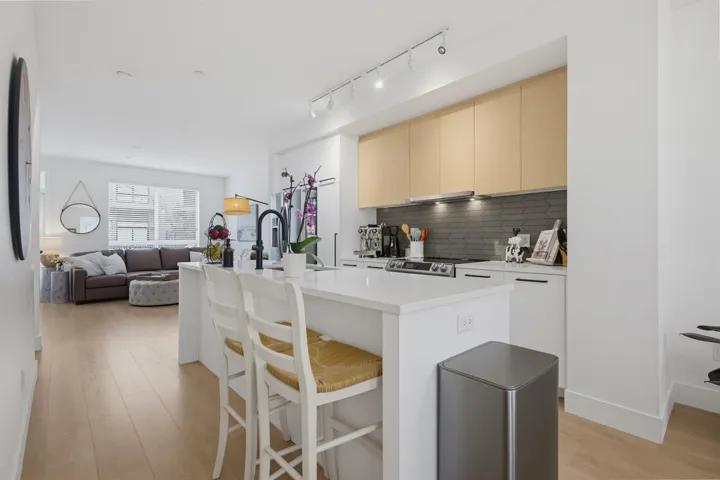 Contemporary kitchen featuring light wood-finish upper cabinetry, white lower cabinetry with matte black hardware, and an arrow pattern tile backsplash