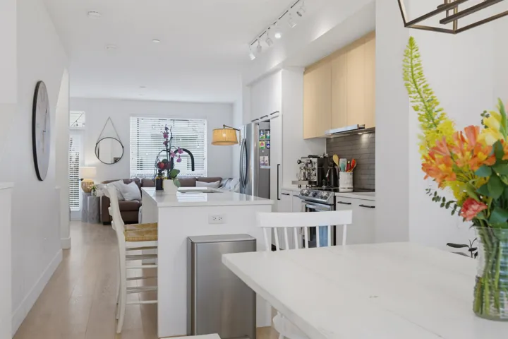 Open-concept kitchen featuring a spacious island with seating, light wood-finish flooring, white cabinetry, integrated stainless steel appliances, and a tiled backsplash
