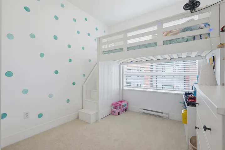 Bright room with plush carpeting, a large window featuring horizontal blinds, and a built-in shelving unit