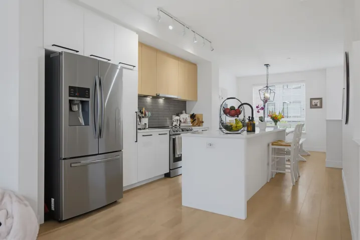 Contemporary kitchen featuring stainless steel appliances, light wood-finish flooring, white cabinetry, a kitchen island with seating, and track lighting