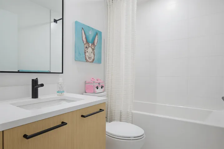 Modern bathroom featuring a wood-finish vanity with matte black hardware, integrated sink, and an undermount tub