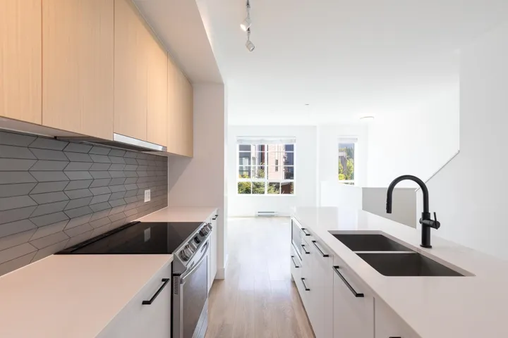 Kitchen featuring light wood-finish cabinetry, a geometric tile backsplash, stainless steel range, and a dual basin undermount sink with a matte black faucet