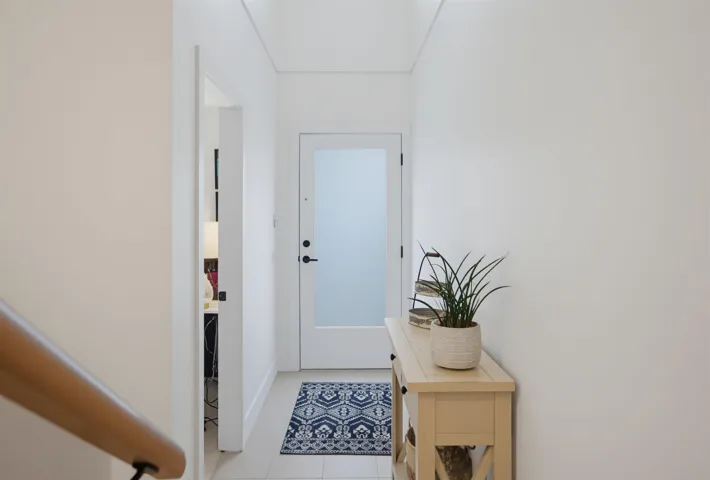 Bright living area featuring wood-finish flooring, white walls, and abundant natural light from multiple windows and a glass door