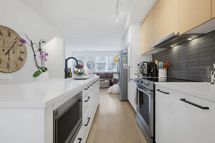 Contemporary kitchen featuring white cabinetry with black hardware, light wood-finish flooring, and a large center island with integrated microwave