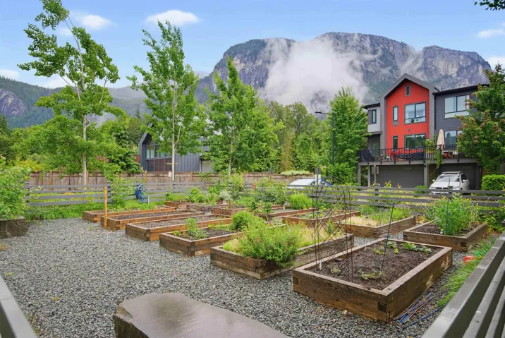 Expansive outdoor space featuring multiple raised garden beds, gravel ground cover, and a substantial stone bench