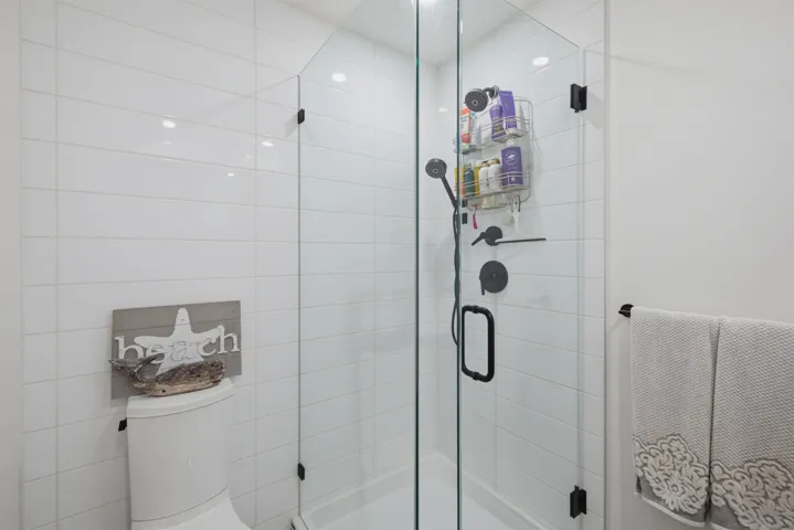 Bathroom featuring a corner glass-enclosed shower with matte black framing, a white vanity with integrated sink and matte black faucet, and a toilet