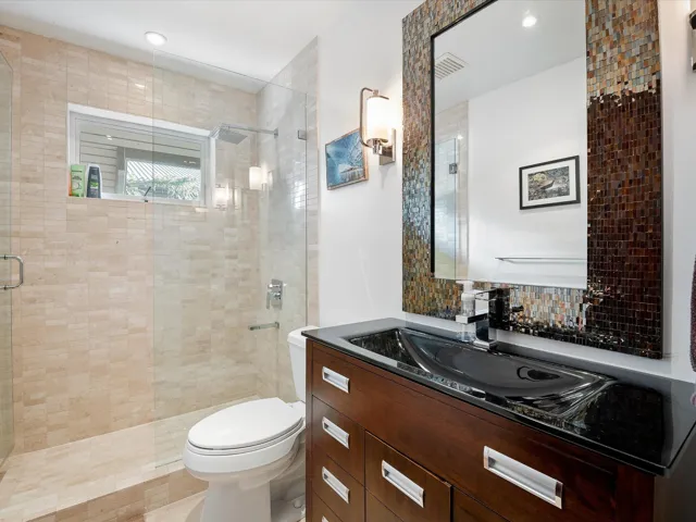 Full bathroom featuring a tile shower, decorative backsplash, visible vents, toilet, and vanity