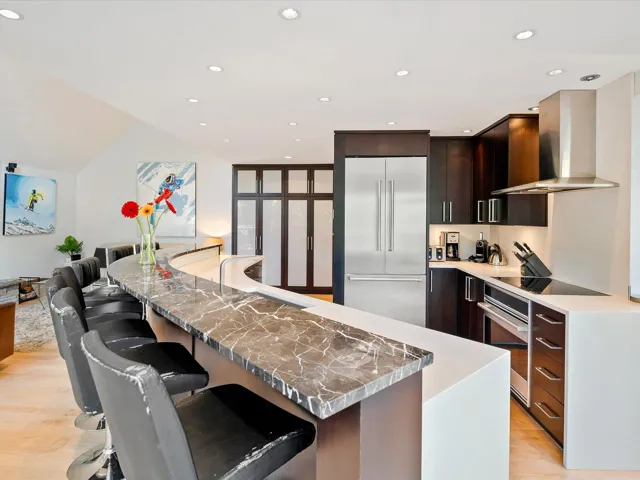 Kitchen with a breakfast bar area, appliances with stainless steel finishes, light wood finished floors, wall chimney exhaust hood, and modern cabinets