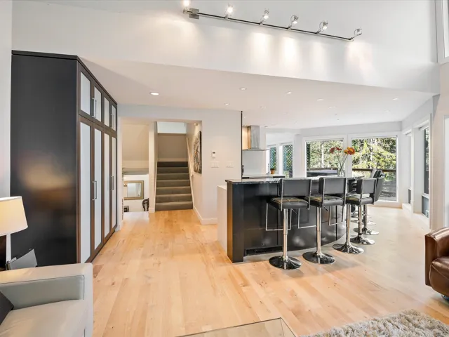 Kitchen featuring wall chimney range hood, light wood-style flooring, a breakfast bar, baseboards, and recessed lighting