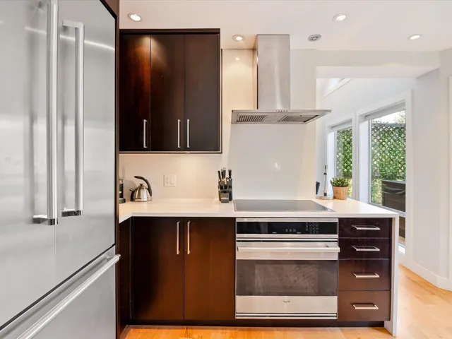 Kitchen with modern cabinets, wall chimney range hood, stainless steel appliances, and light countertops
