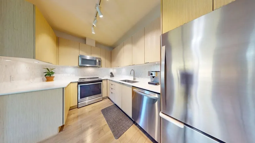 Kitchen with tasteful backsplash, stainless steel appliances, light countertops, light wood finished floors,