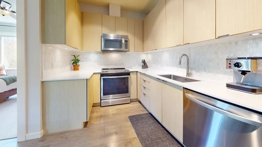 Kitchen featuring a sink, decorative backsplash, stainless steel appliances, light wood-style flooring, and light countertops