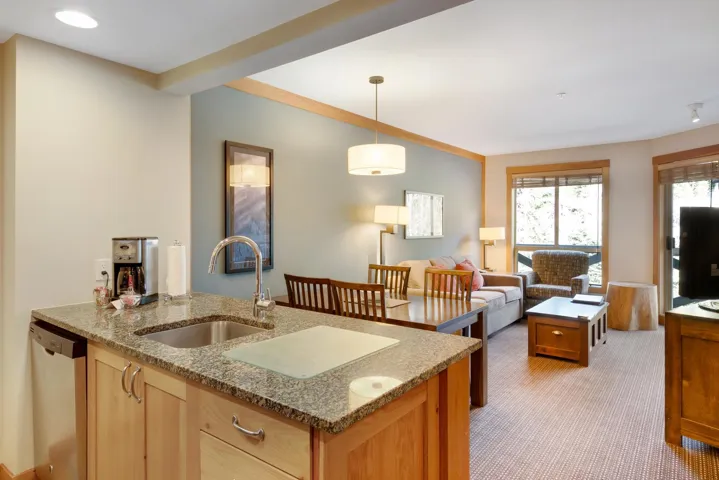 Kitchen featuring light carpet, a sink, stainless steel dishwasher, light stone countertops, and pendant lighting