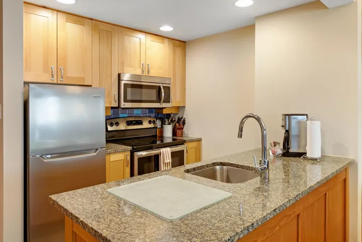Kitchen with appliances with stainless steel finishes, light stone countertops, light brown cabinets, a sink, and recessed lighting