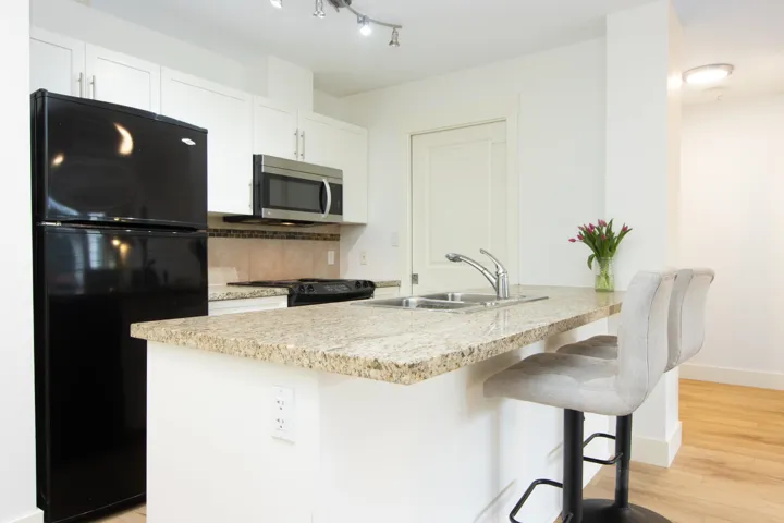 Kitchen with light stone countertops, light wood-style floors, white cabinets, a sink, and black appliances