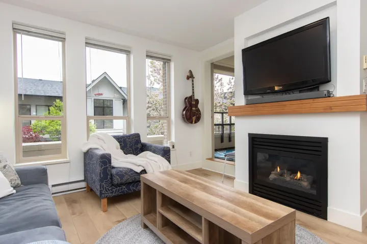 Living area featuring light wood-style floors, a baseboard radiator, a glass covered fireplace, and a healthy amount of sunlight