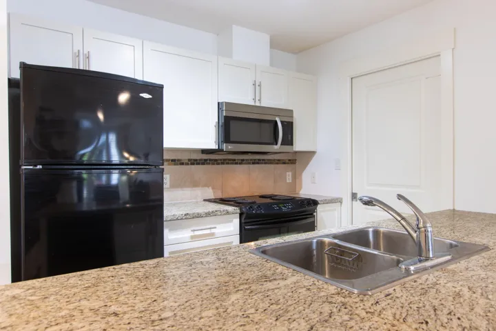 Kitchen featuring light stone counters, a sink, white cabinetry, backsplash, and black appliances