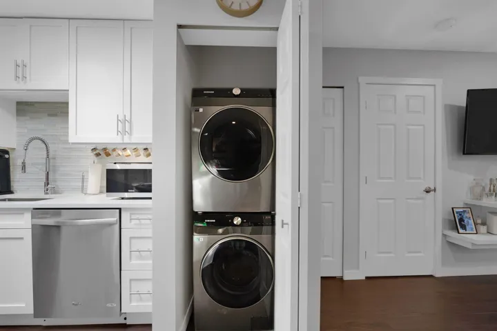 Laundry area with stacked washer / drying machine and dark wood finished floors